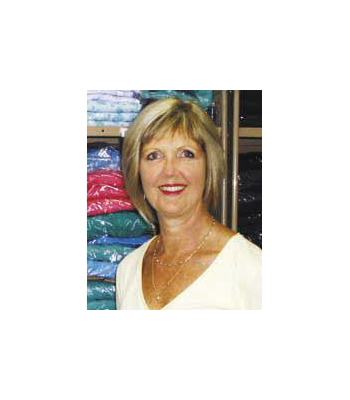 Linda Dugan, owner of Petal Back Clothing, standing in her store. She is white, with blond hair, and is wearing a white top.