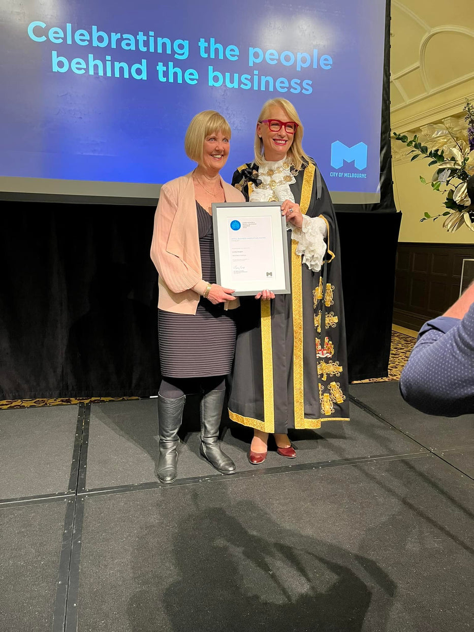 Petal Back owner Linda is on stage receiving a framed Lord Mayor's Award from Sally Capp, who is dressed in black and gold mayoral robes.